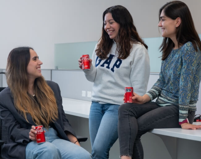 mujeres hablando con latas de coca-cola en las manos